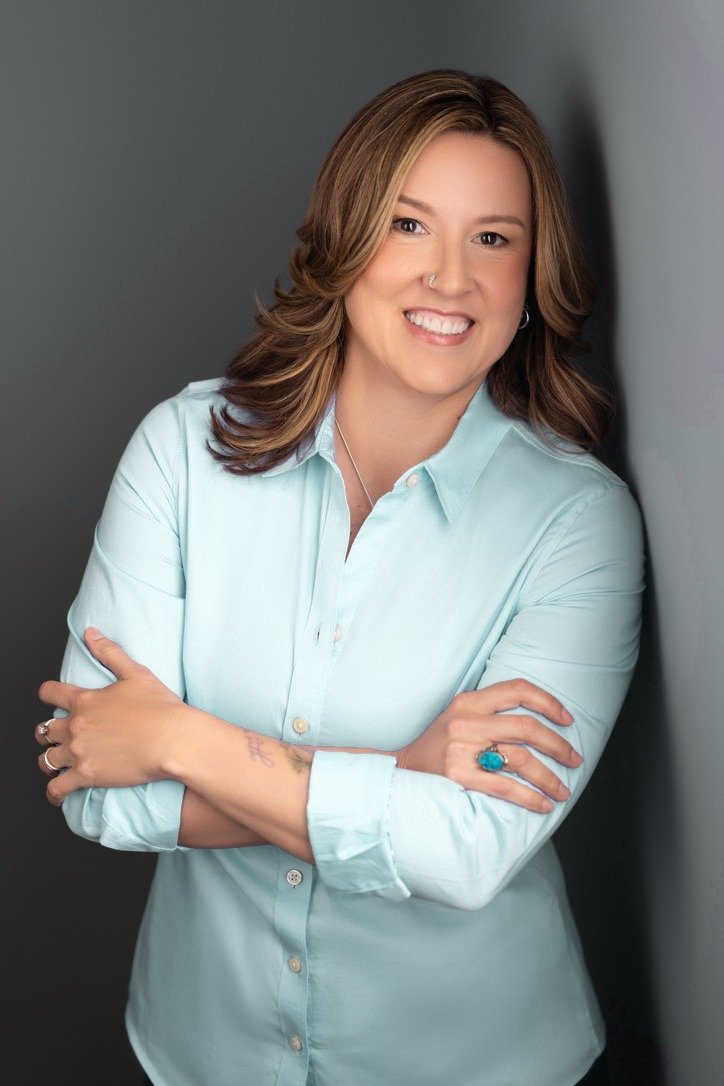 Jenn McDaigle, smiling with her arms crossed, in a light button-down shirt