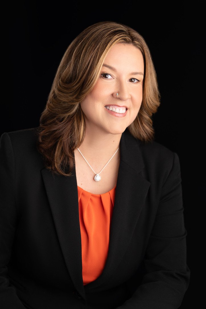 Portrait of Jenn McDaigle in a black blazer and orange blouse